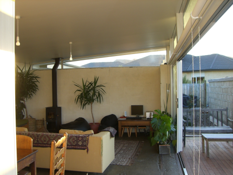 Earth House — living area with wood burner opening to the deck